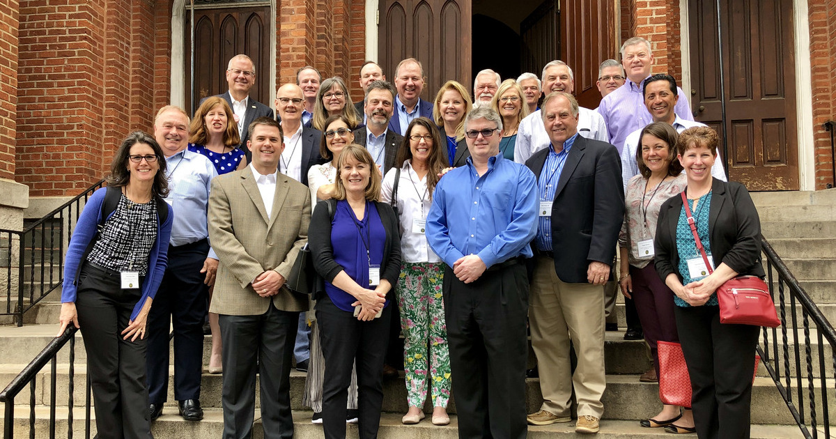 A panel of four speakers sits on a stage in front of an audience