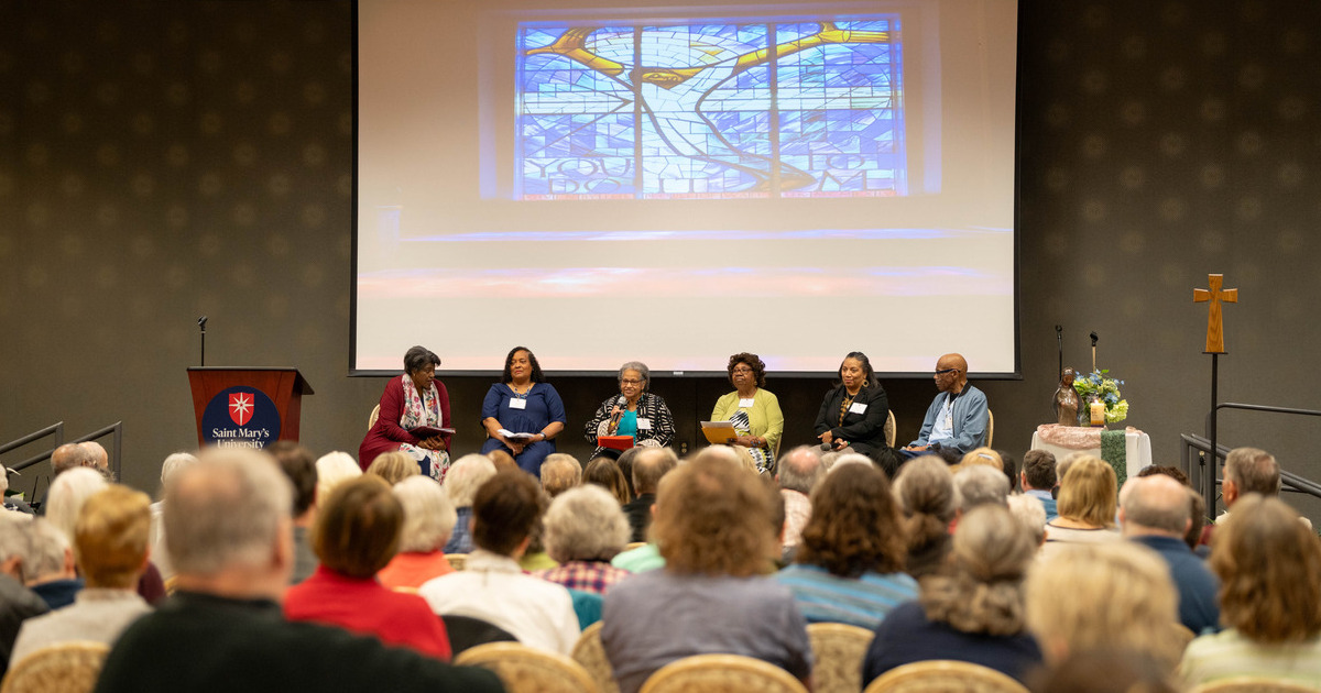 A panel of speakers who are Black sit on stage in front of an audience