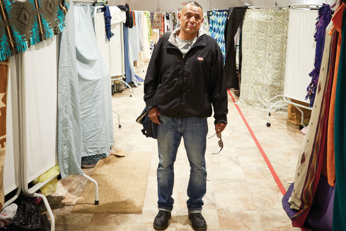 A resident stands in the Navigation Center hallway, framed by hanging sheets and blankets.