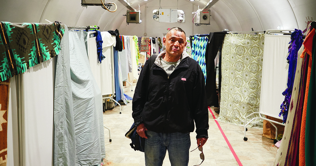A man carrying a bag stands in the middle of a temporary shelter